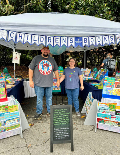 A couple holding hands at their booth with vraious childrens‘ books.
