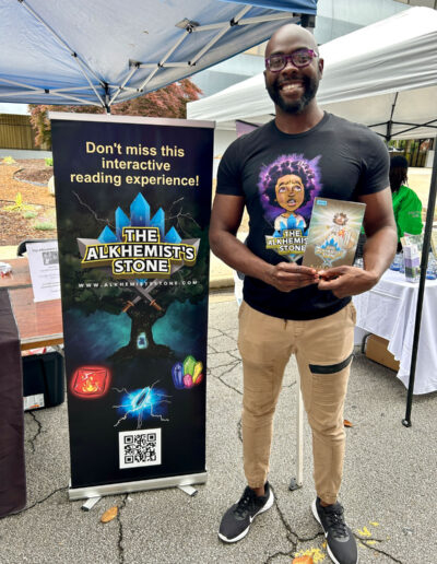 An African American man showing off his children’s book titled “The Alkhemist’s Stone”