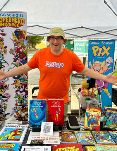 A friendly, smiling man posing in front of his booth that displays comic books.